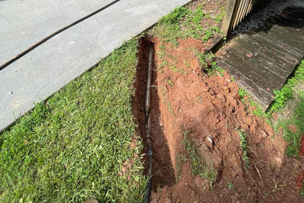 Underground pipe exposed in a narrow trench beside a driveway