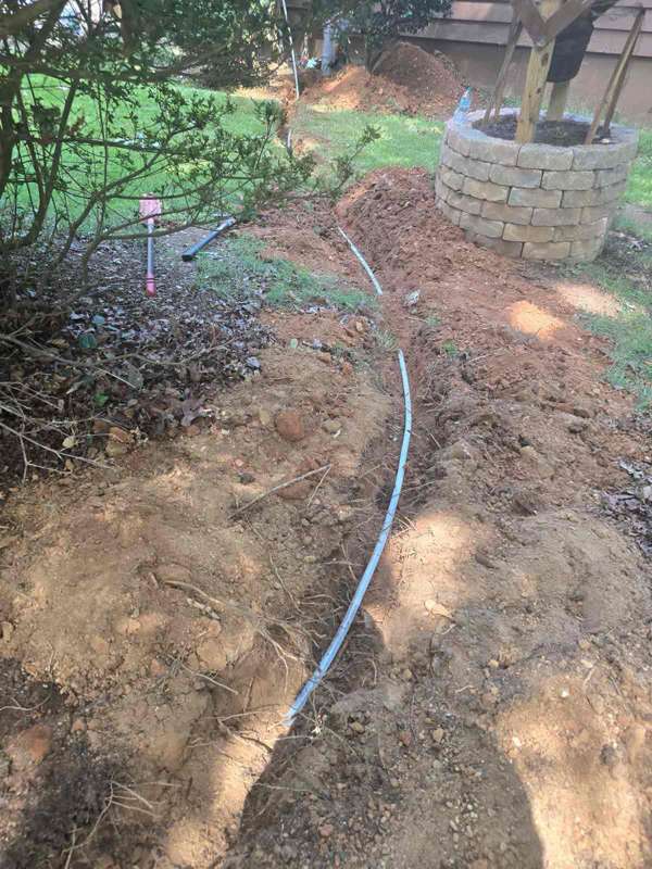 Water supply line exposed in a yard trench beside a stone planter