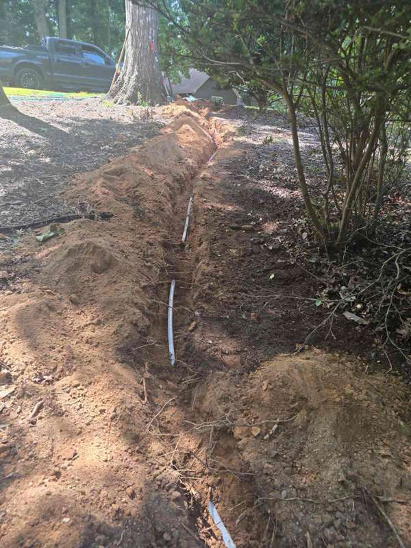 Exposed water line running through a narrow yard trench